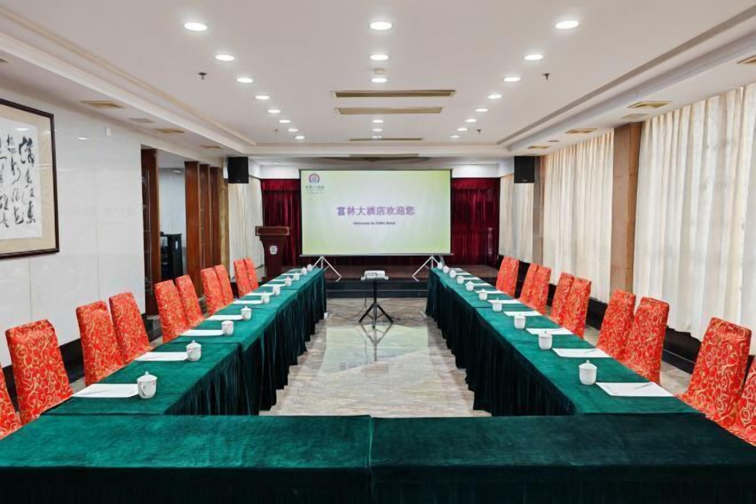 A conference room with a long table, red patterned chairs, and a projection screen at the front.