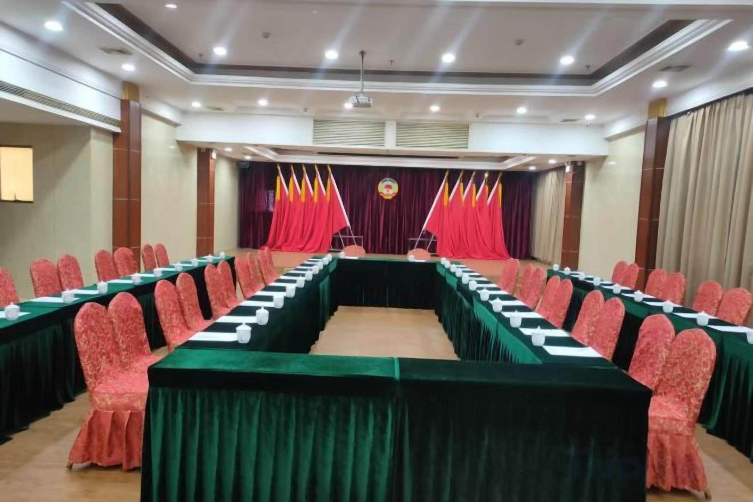 A conference room with a long table, red chairs, and a stage with curtains.