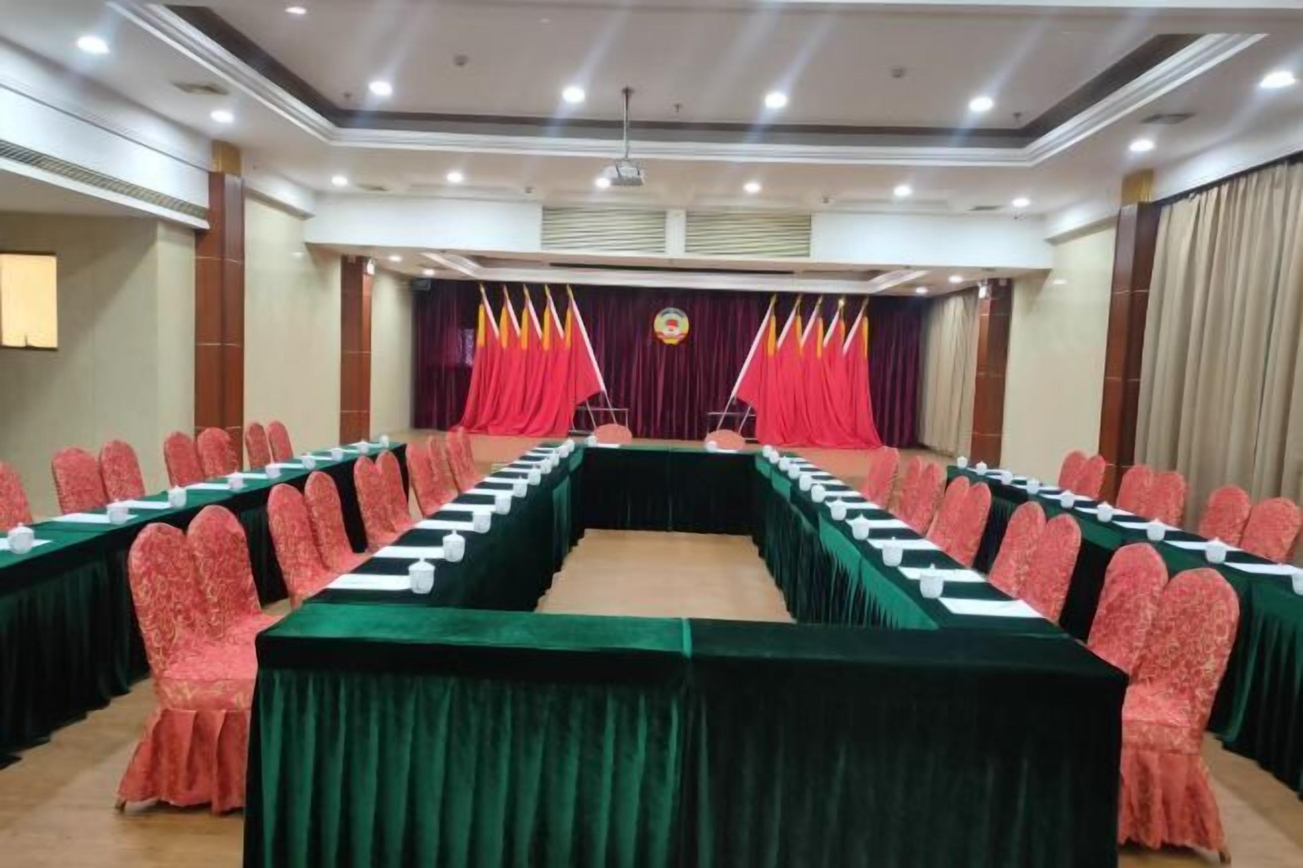 A conference room with a long table, red curtains, and flags.