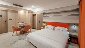 A hotel room with a bed, a desk with chairs, a wall-mounted TV, and a mountain landscape mural. - Fulin Hotel (Huilai)