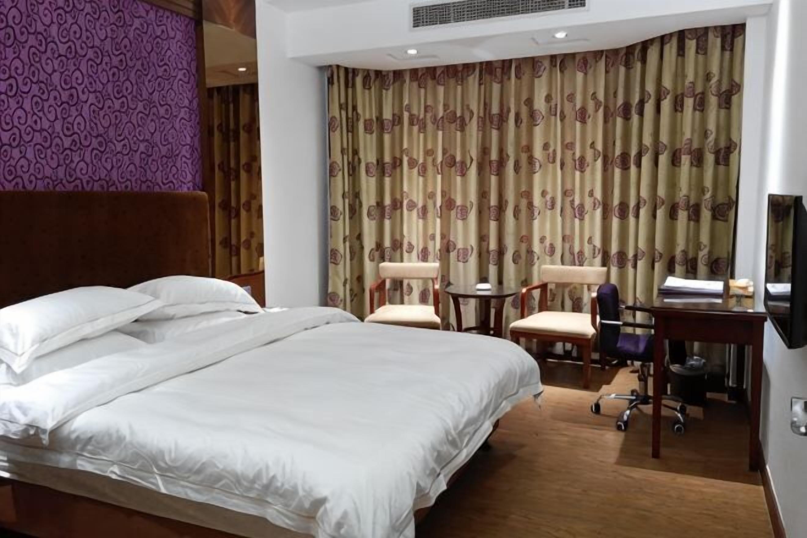 Hotellihuone, jossa on sänky, kaksi tuolia, pieni pöytä ja työpöytä tuolilla.