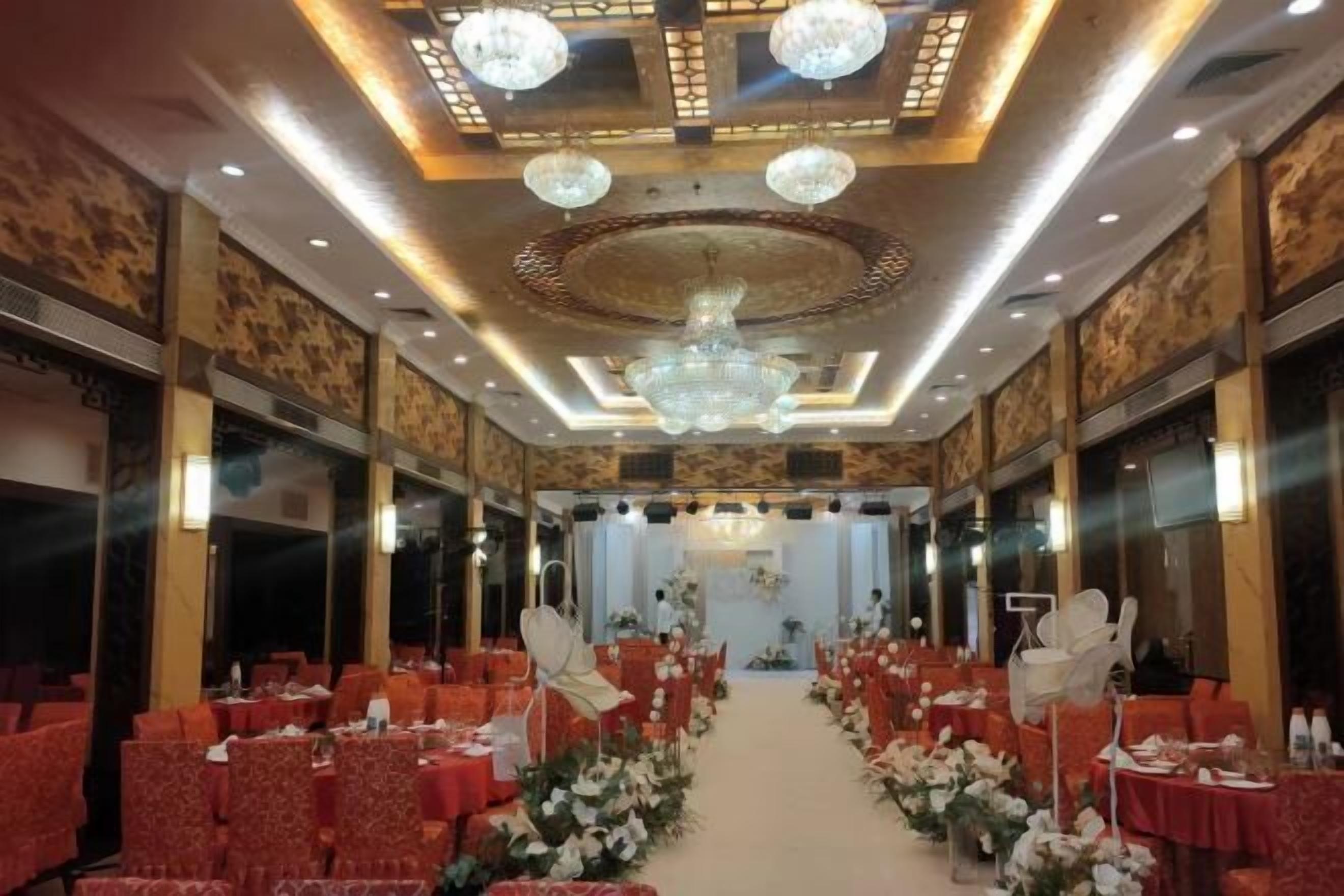 A banquet hall with rows of tables and chairs, a central aisle, and decorative lighting fixtures.