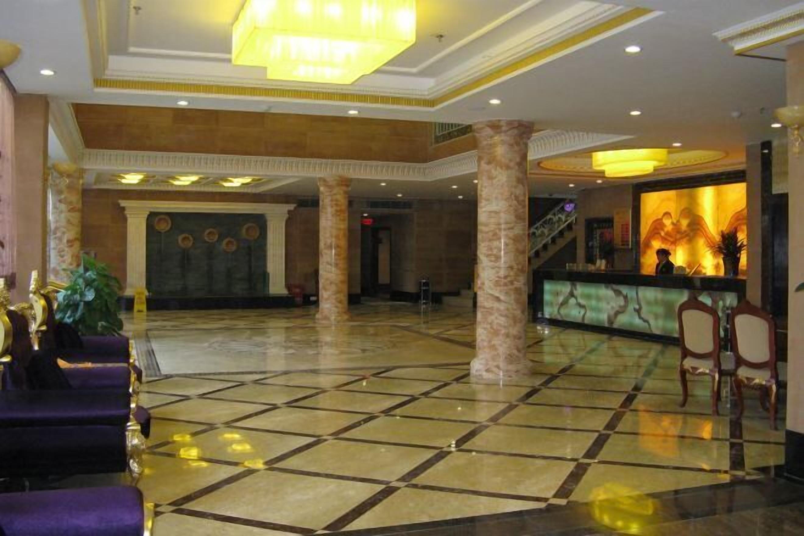 A spacious lobby with a check-in counter, marble columns, and a chandelier.