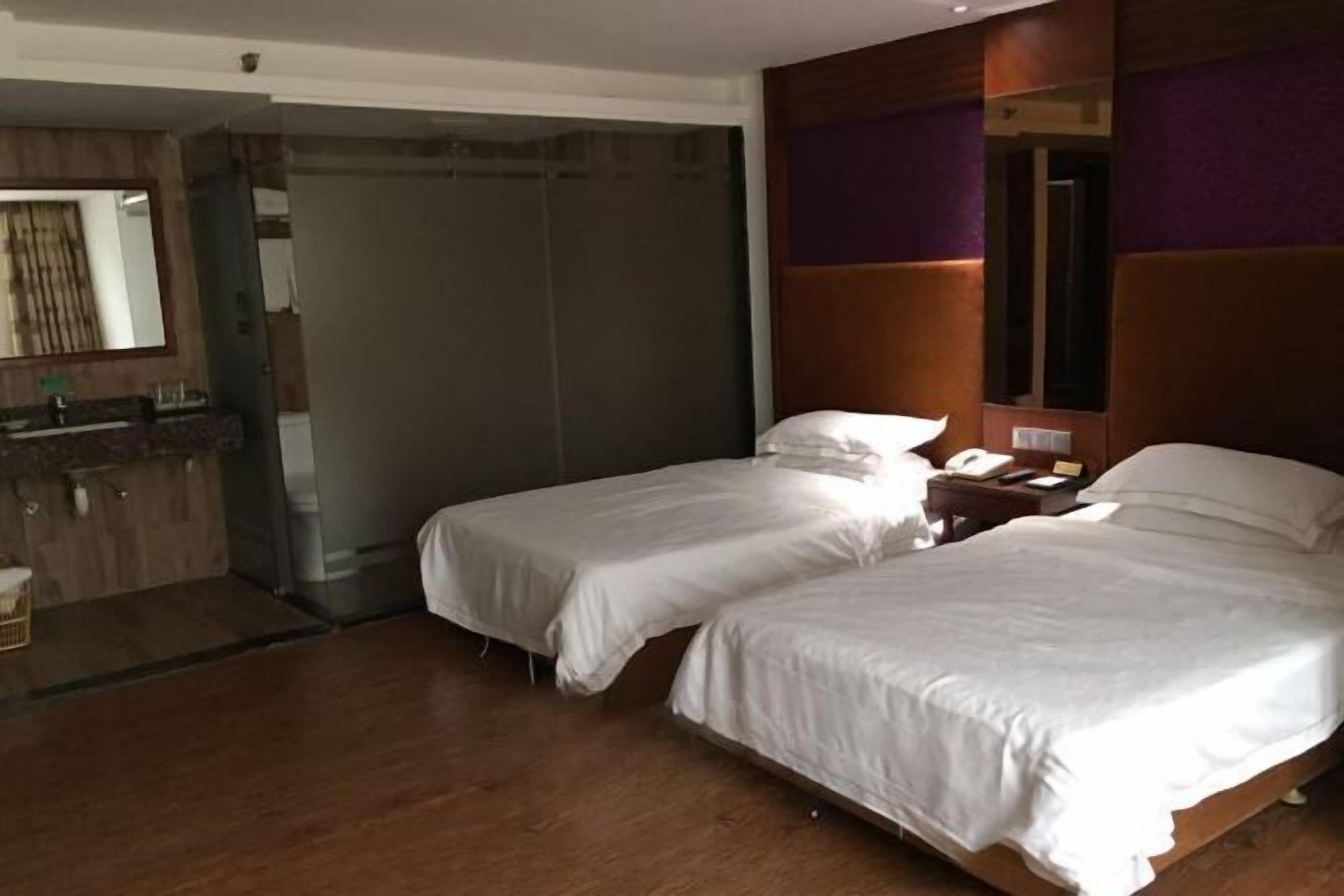 A hotel room with two single beds, a bathroom with a shower, and a small desk with a phone and lamp.
