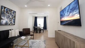 Una sala de estar moderna con una mesa de centro de vidrio, un sofá negro y un televisor de pantalla plana grande en la pared.