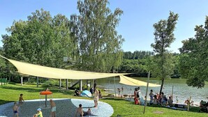 Un parque con una zona de juegos acuáticos, un área de descanso cubierta y un lago.