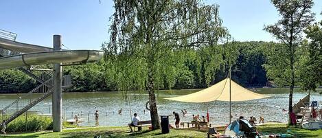 Un parque junto al lago con zona de picnic, área de juegos y espacio para nadar.