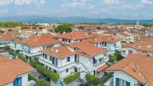 Un quartiere residenziale con case dalle facciate bianche e tetti in tegole rosse, immerso nel verde e con montagne sullo sfondo.