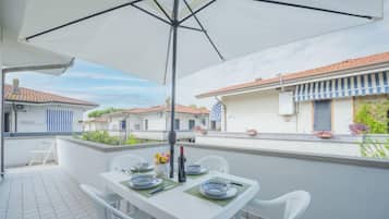 A balcony with a table set for two, white chairs, and a large umbrella.