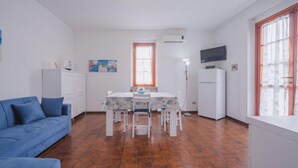 Un ambiente compatto con angolo pranzo, divano, televisione e finestra con tende.
