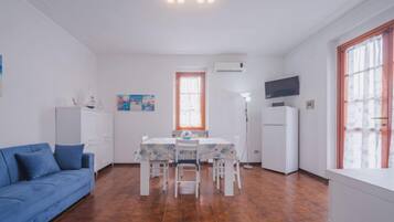 A compact living space with a dining area, a sofa, a TV, and a window with curtains.