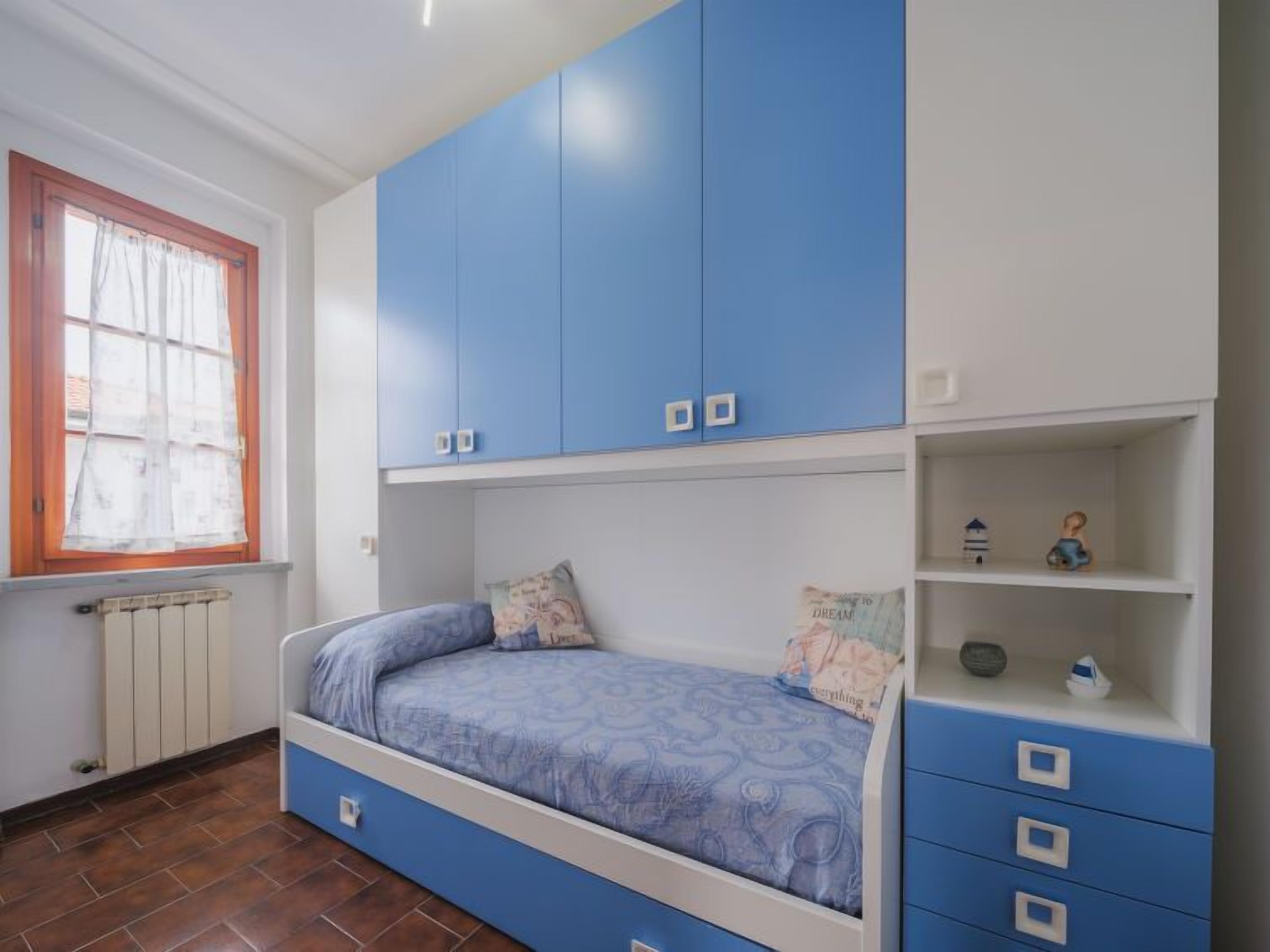 A bedroom with a bed, blue cabinets, a radiator, and a window with curtains.