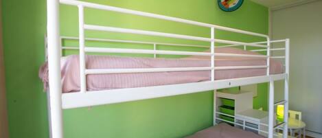 A bunk bed with a lower bunk and a single bed, green walls, a small table with a lamp, and a clock on the wall.