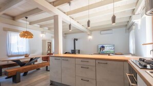 A modern kitchen with wooden beams, a central island with drawers, pendant lighting, and a television.