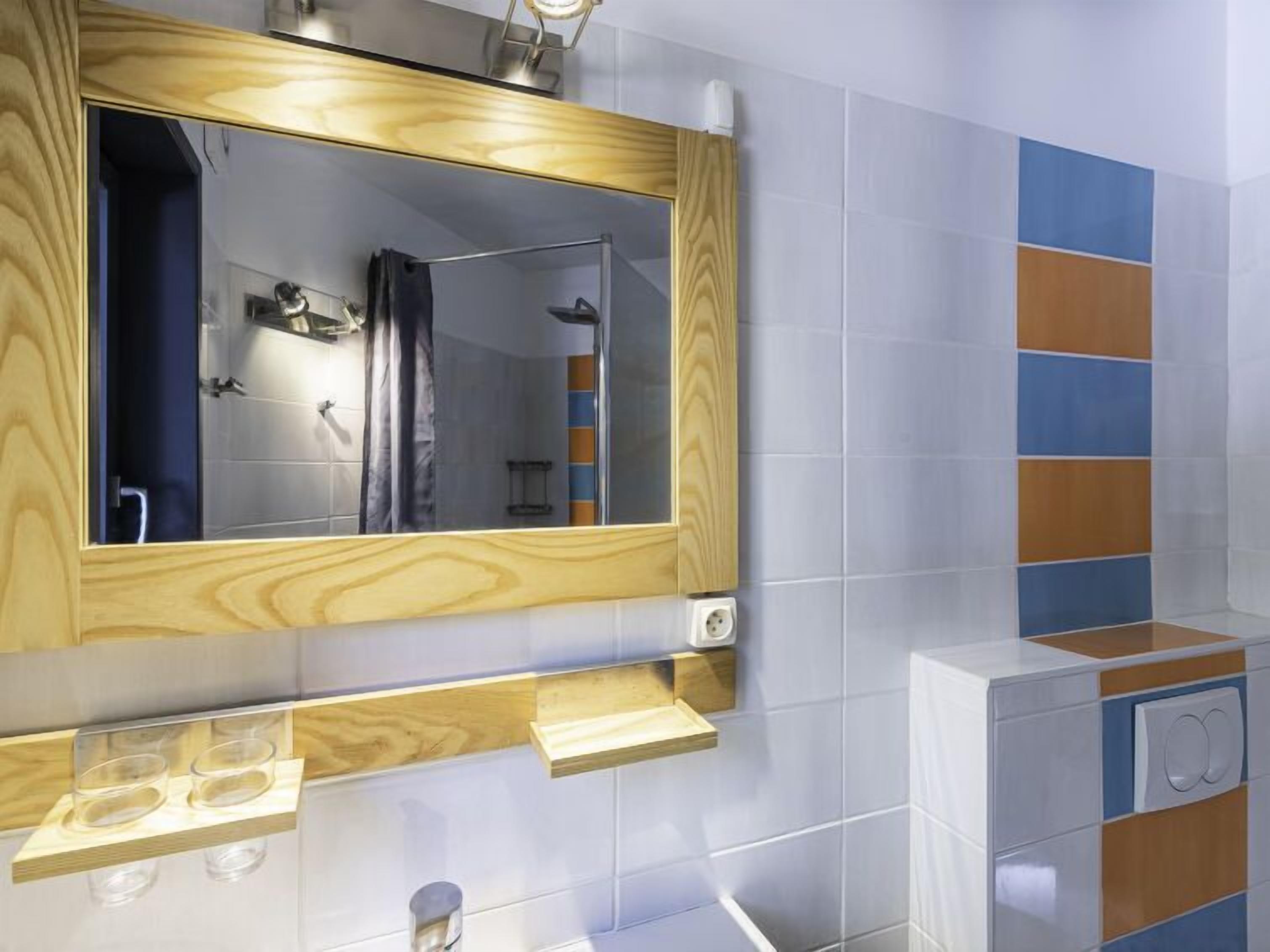 A modern bathroom with a wooden vanity, a large mirror, and a tiled wall with blue and orange accents.