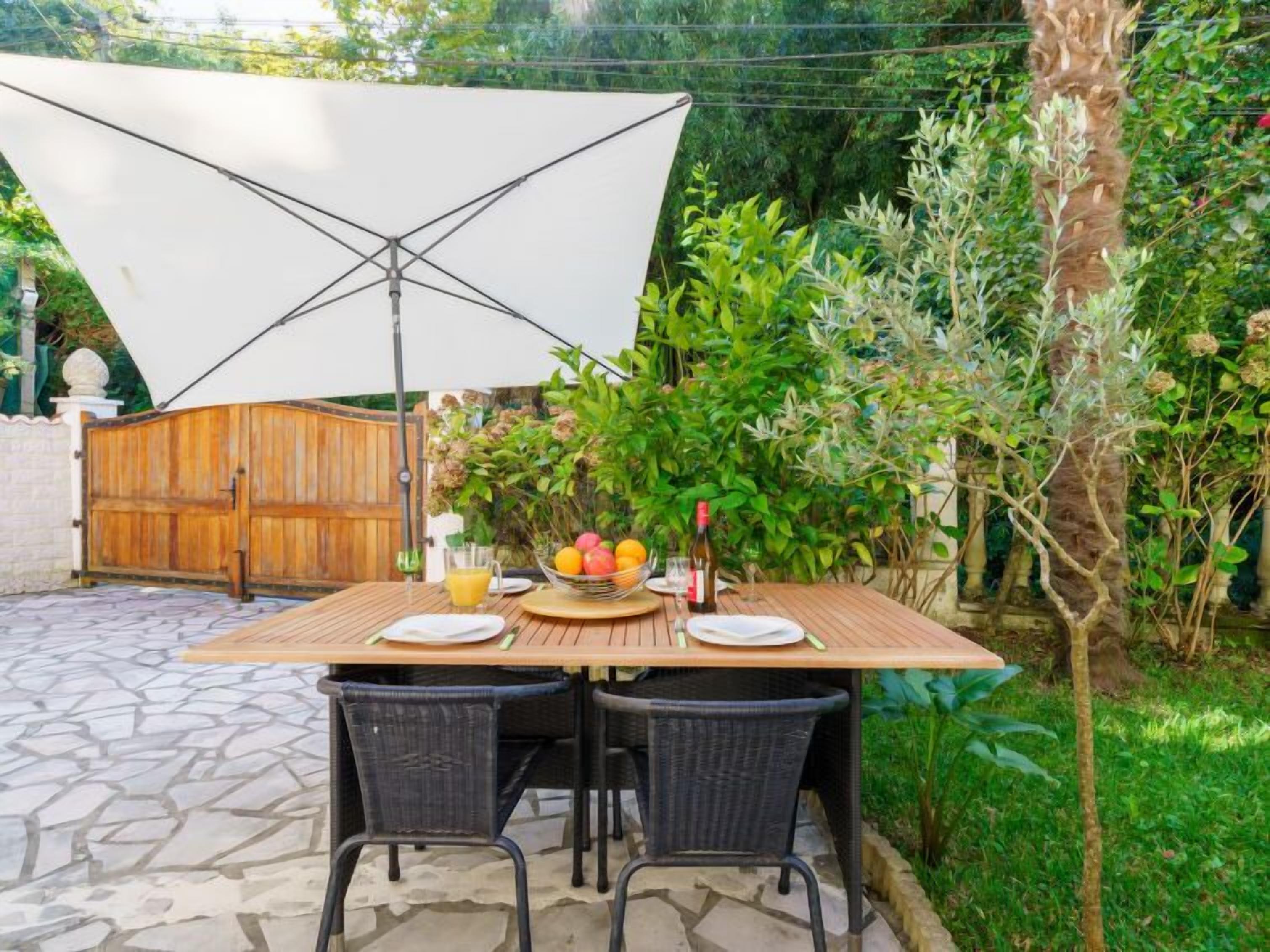 Eine Terrasse im Freien mit einem Holztisch, gedeckt für zwei Personen, umgeben von Steinböden und schwarzen Korbstühlen.