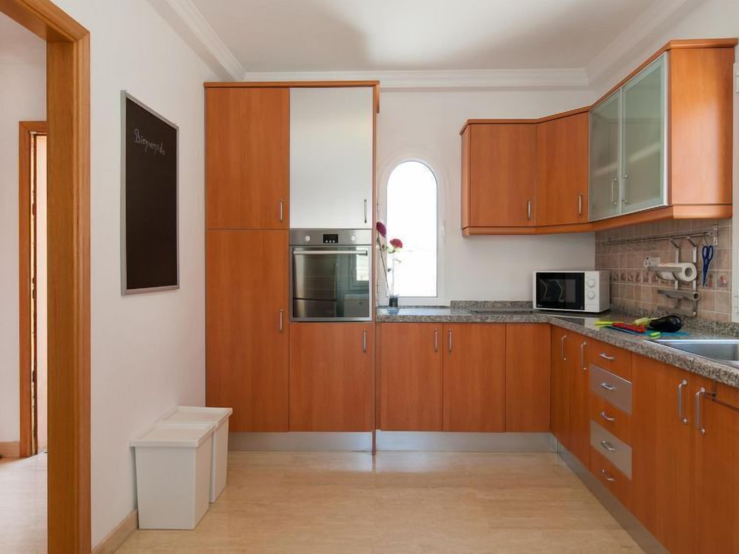Una cocina moderna con armarios de madera, electrodomésticos de acero inoxidable y una pequeña encimera con microondas.