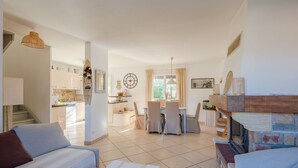 A spacious living area with a dining table, chairs, and a fireplace. There is a kitchen in the background with modern appliances and a staircase leading to another level. - Le Laurier by Interhome (Sainte Maxime)