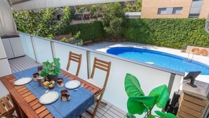 An outdoor patio with a table set for dining, overlooking a swimming pool and a landscaped garden. - Apartment Silves by Interhome (Tossa de Mar)