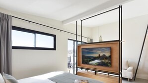 Ein modernes Hotelzimmer mit einem großen Bett, einem an einem Holzbalken befestigten Fernseher und einem Fenster mit Blick ins Freie.