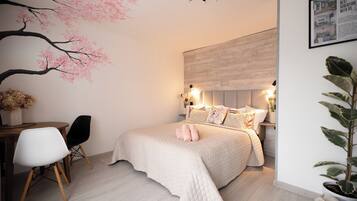 A bedroom with a bed, bedside tables, a desk, chairs, and a wall-mounted light fixture.