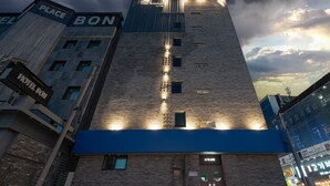 Een hoog hotelgebouw met een opvallend 'Place Bon' bord en een 'Hotel Bon' bord aan de linkerkant.