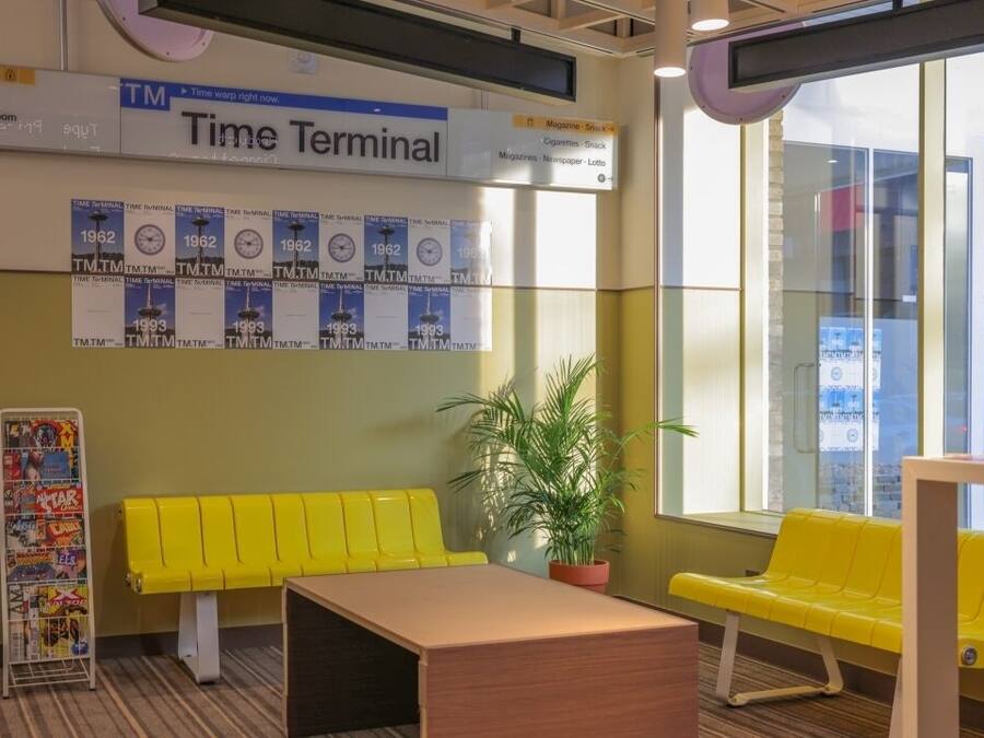 A Time Terminal with a yellow bench, a potted plant, and a wall displaying Time Terminal posters from 1962 and 1993.