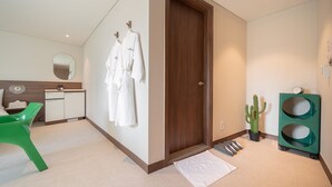 Een moderne badkamer met een houten deur, een groene stoel, een spiegel en een cactus.