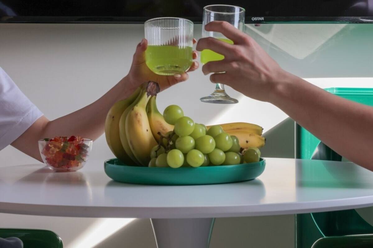 A table with a bowl of fruit, a plate of bananas and grapes, and two glasses of a yellow beverage.