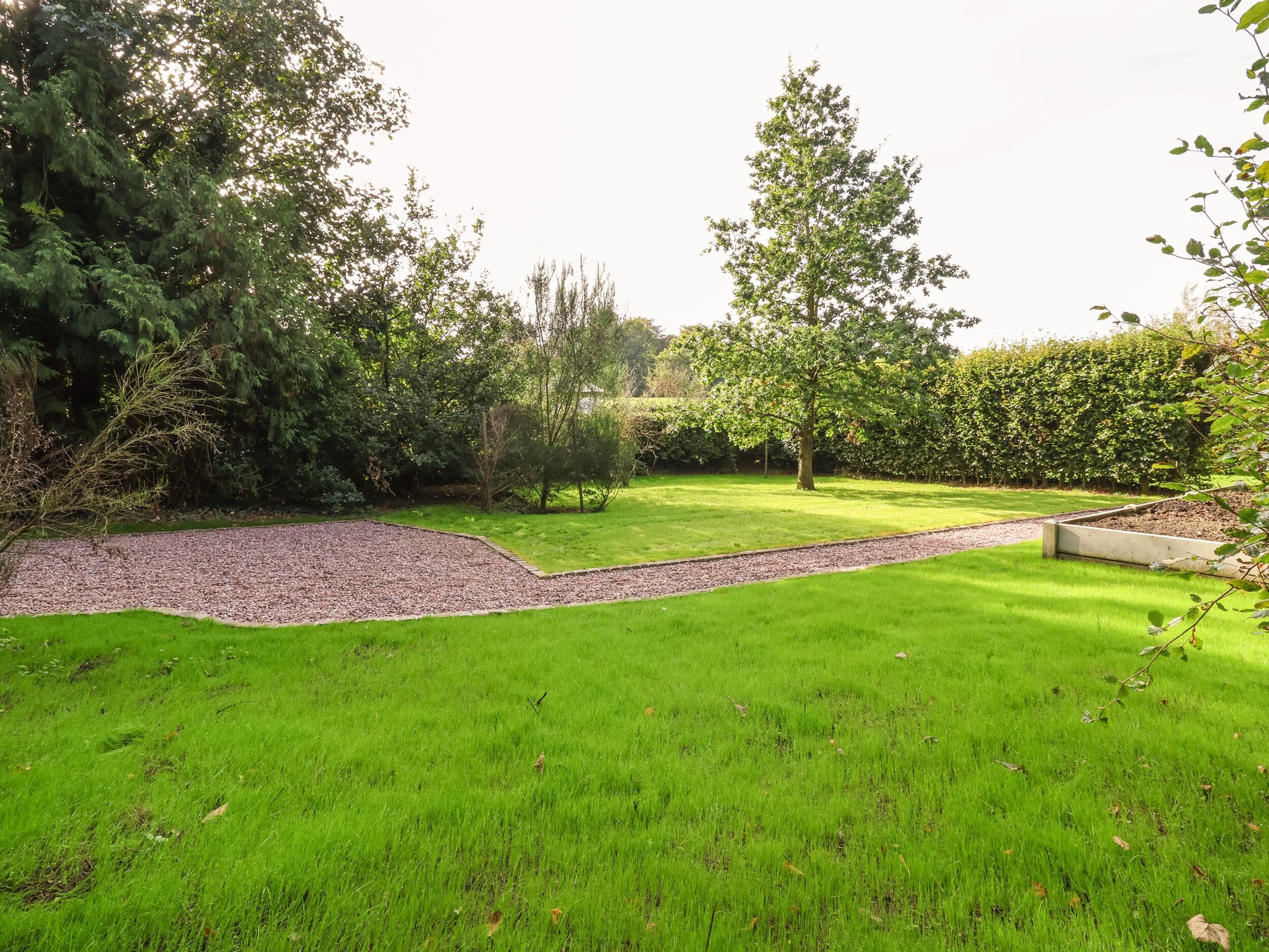 A well-maintained garden with a variety of trees and shrubs, a gravel path, and a neatly trimmed lawn.