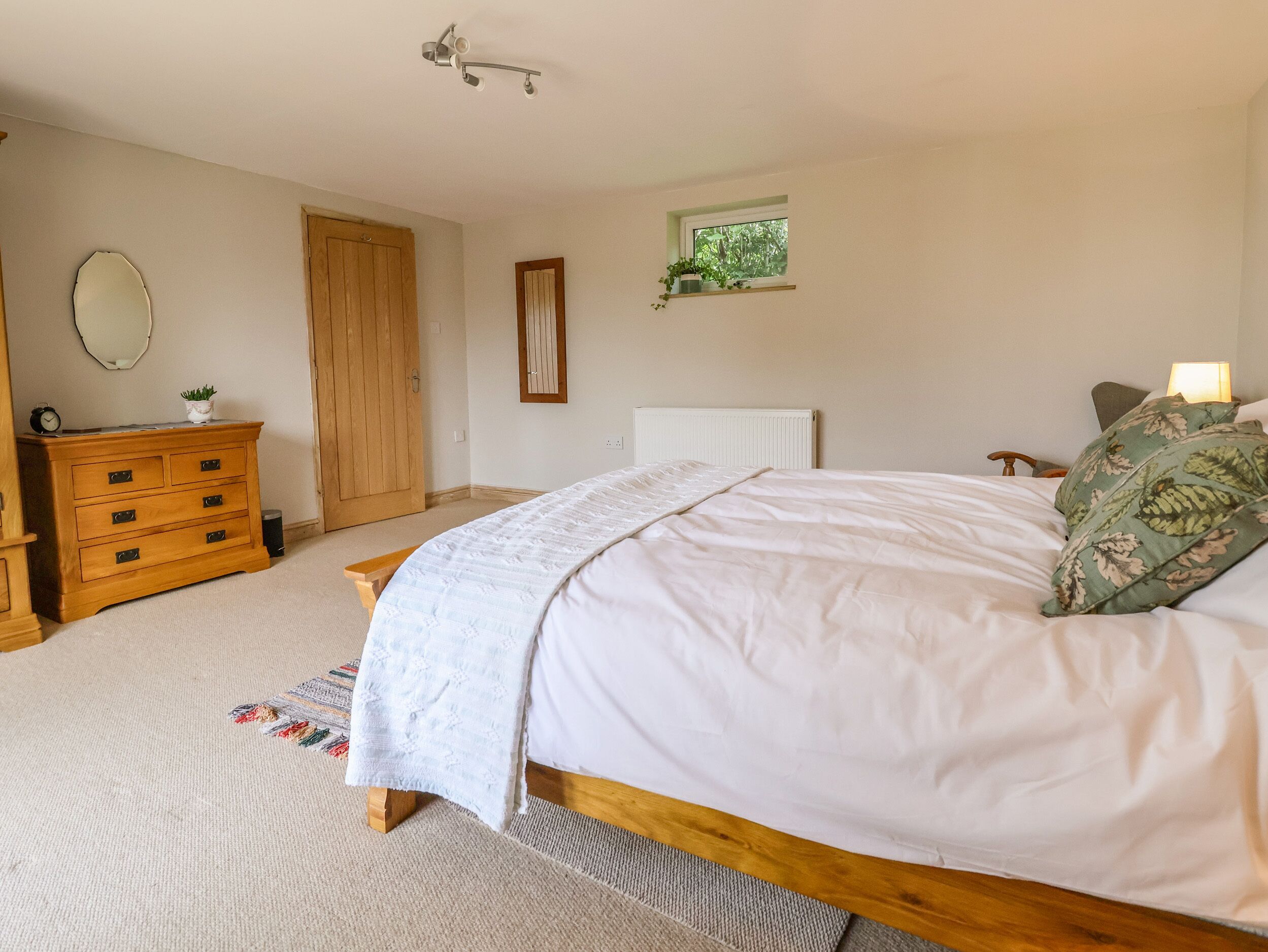 A bedroom with a bed, wooden dresser, and a small window with a plant.