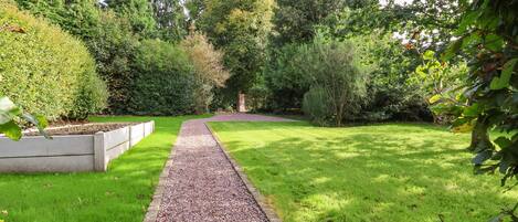 A gravel pathway leading through a well-maintained garden with various shrubs and trees.