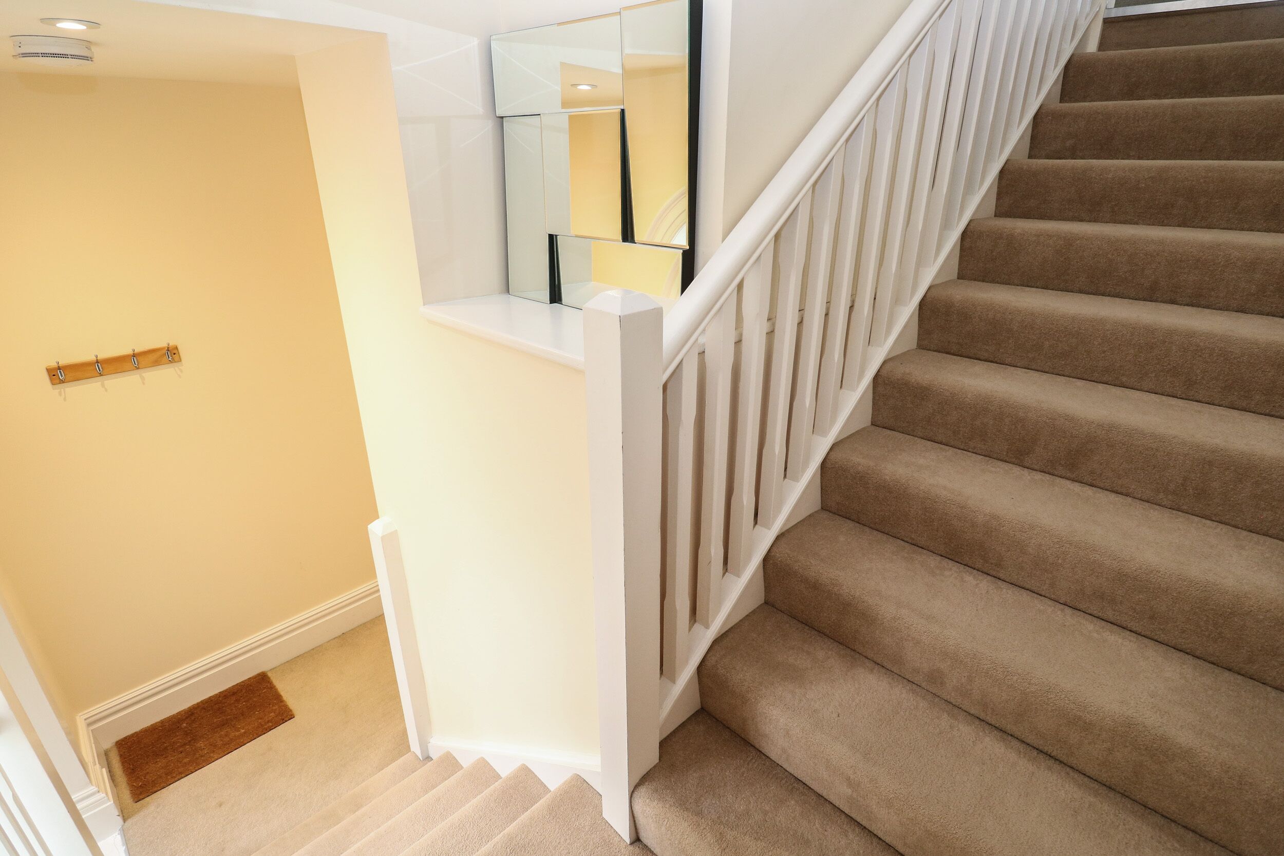 Eine Teppichstufen-Treppe mit weißen Geländern und einer Handlauf, die zu einer Empore mit einem Spiegel und einem Kleiderständer führt.