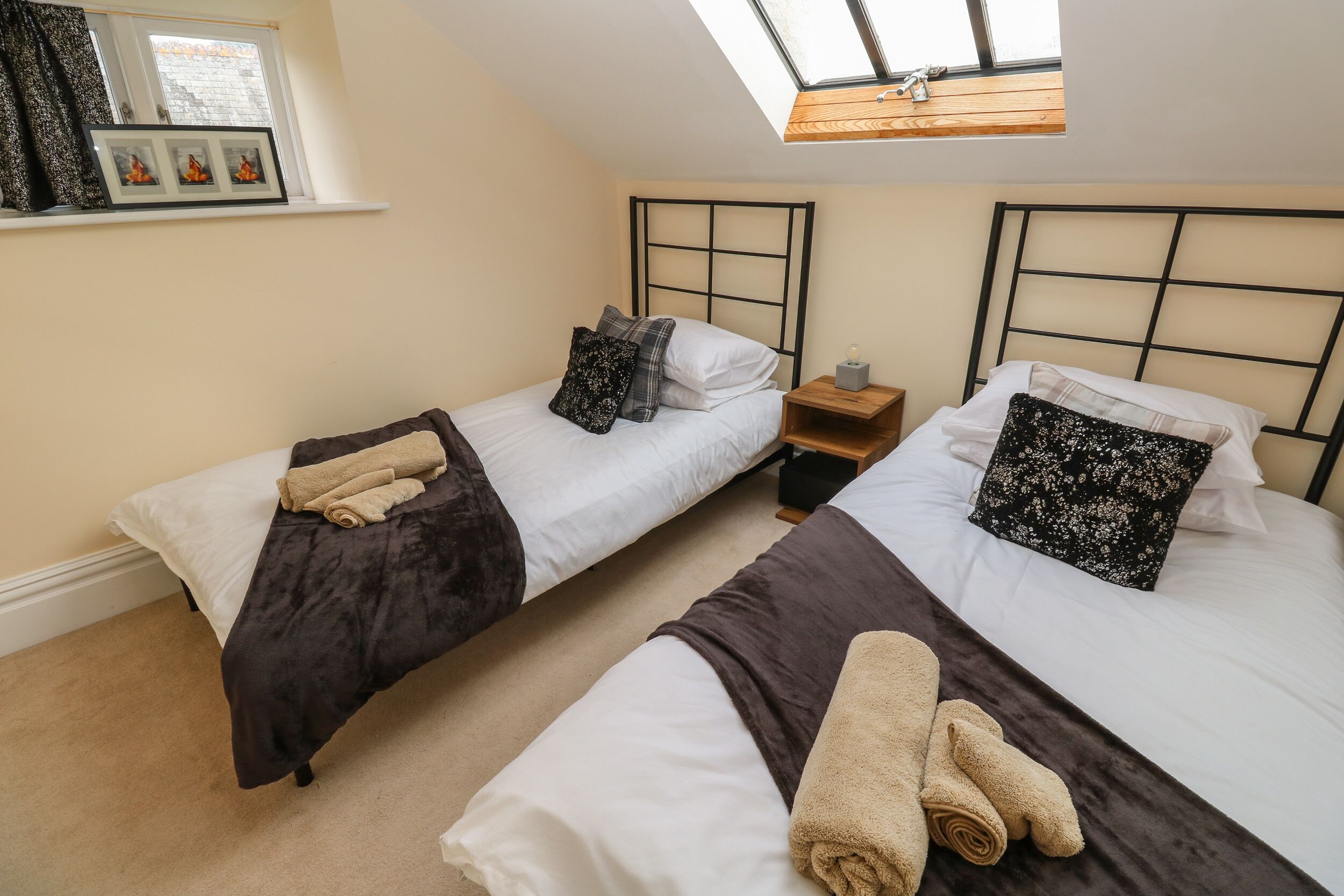 A bedroom with two beds, each with a headboard, a small bedside table, and a window above.