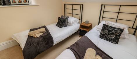 A bedroom with two beds, each with a headboard, a small bedside table, and a window above.