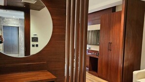 A modern bathroom with a wooden vanity, a round mirror, a blue patterned rug, and a wooden wardrobe. - Four Leaf Hotel Akosha (Varanasi)
