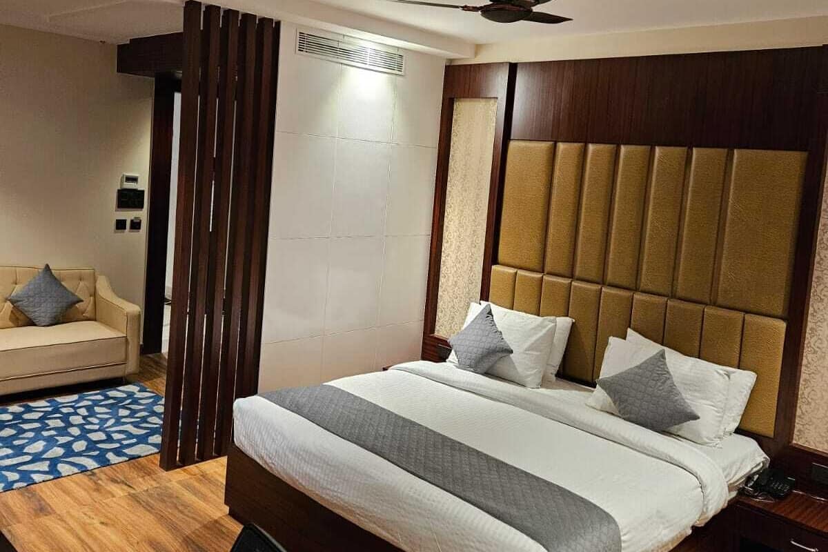 Quarto de hotel com cama, escrivaninha, cadeira, ventoinha no teto e ar condicionado fixado na parede.