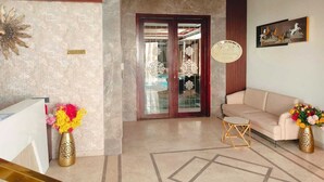 A reception area with a reception desk, a beige sofa, decorative vases, and a patterned floor. - Four Leaf Hotel Akosha (Varanasi)