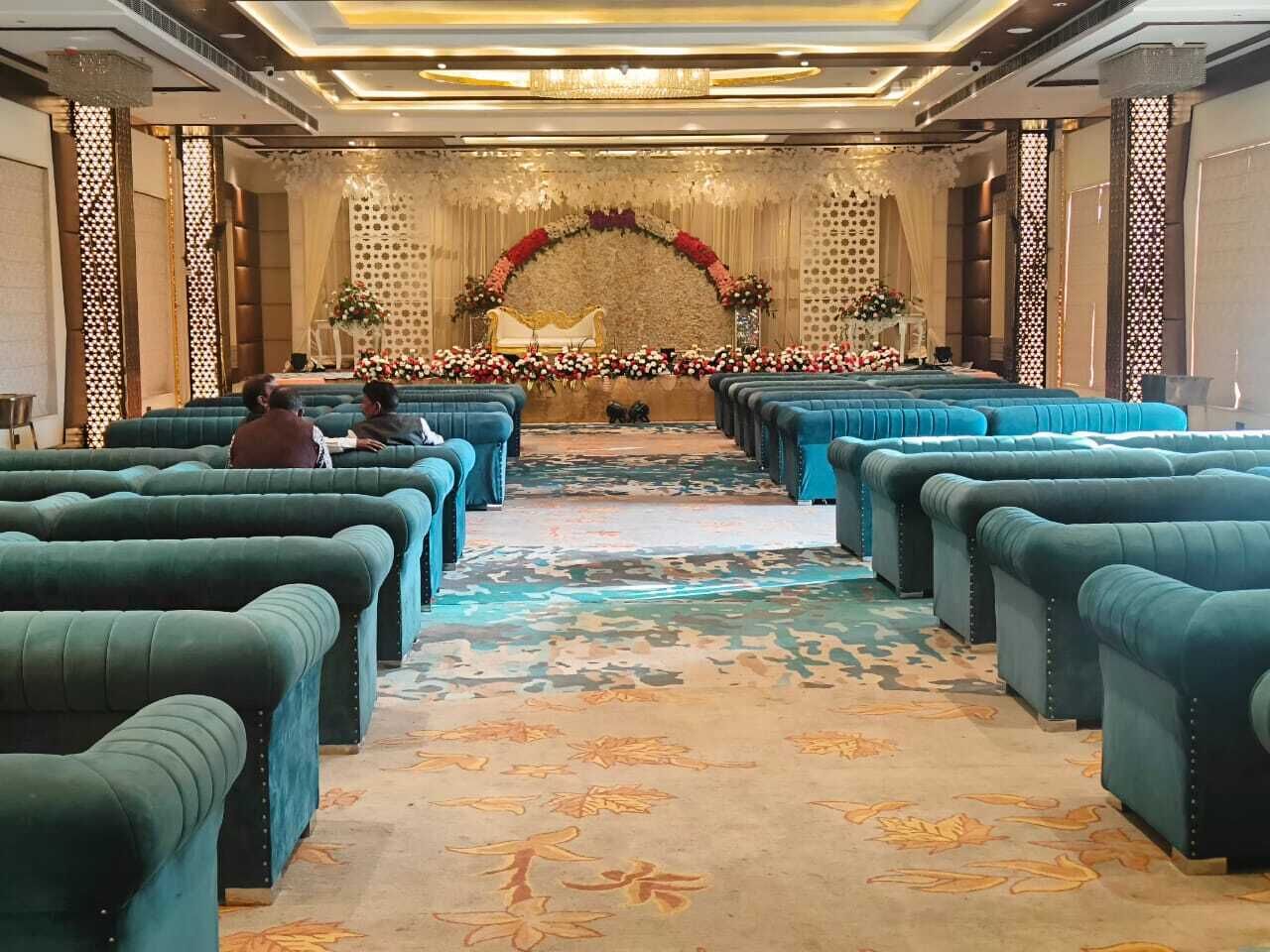 Un hall d’hôtel avec des rangées de sièges bleus et moelleux, une arche décorative ornée de fleurs et un tapis à motifs.