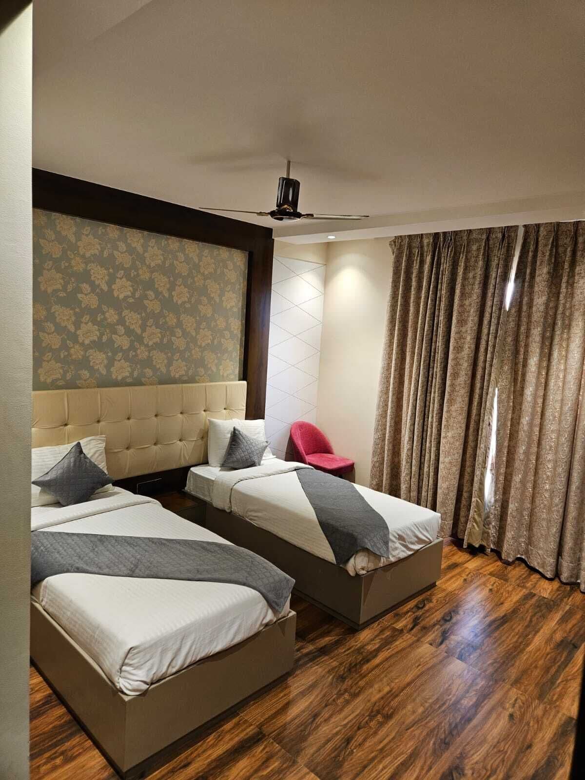A hotel room with two beds, a red chair, a ceiling fan, and a patterned wallpaper.