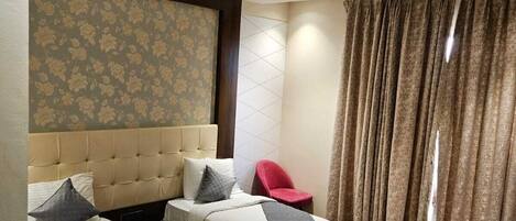 A hotel room with two beds, a red chair, a ceiling fan, and a patterned wallpaper.