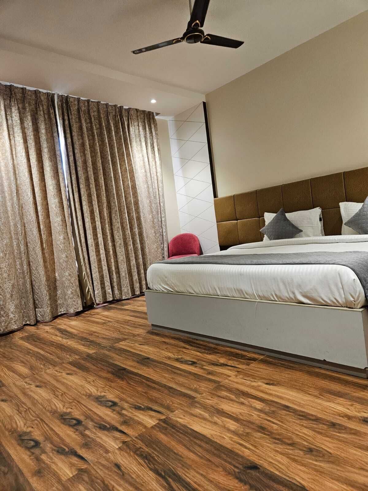 Ein modernes Hotelzimmer mit einem großen Bett, Holzboden, Deckenventilator und Blick ins Freie durch Vorhänge.