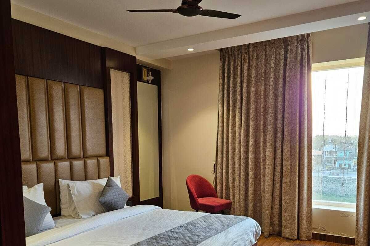 Quarto de hotel com uma cama grande, um ventilador de teto, uma cadeira vermelha e vista para a cidade pela janela.