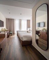 A hotel room with a large bed, a desk with a chair, a mirror, and a television on the wall.
