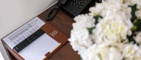 Un escritorio de madera con un teléfono negro, una libreta de cuero marrón y un ramo de flores blancas.