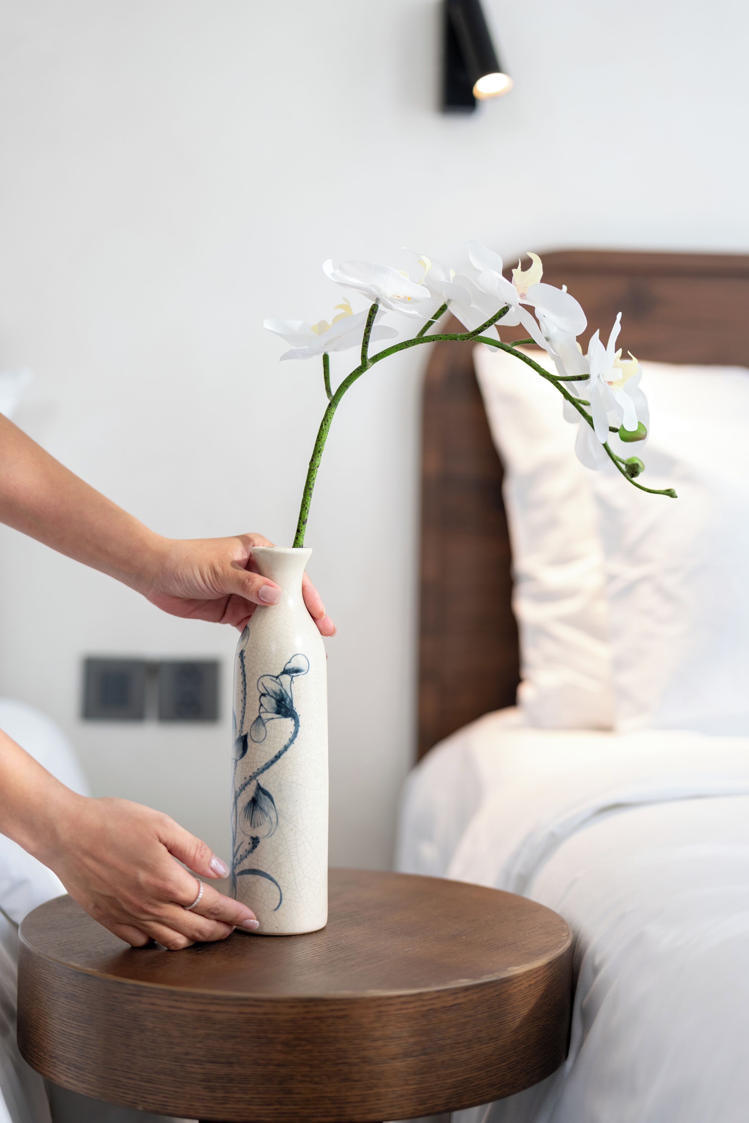 Una mano colocando un jarrón con flores blancas sobre una mesita de madera.