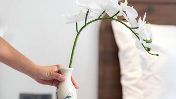 Una mano colocando un jarrón con flores blancas sobre una mesita de madera.
