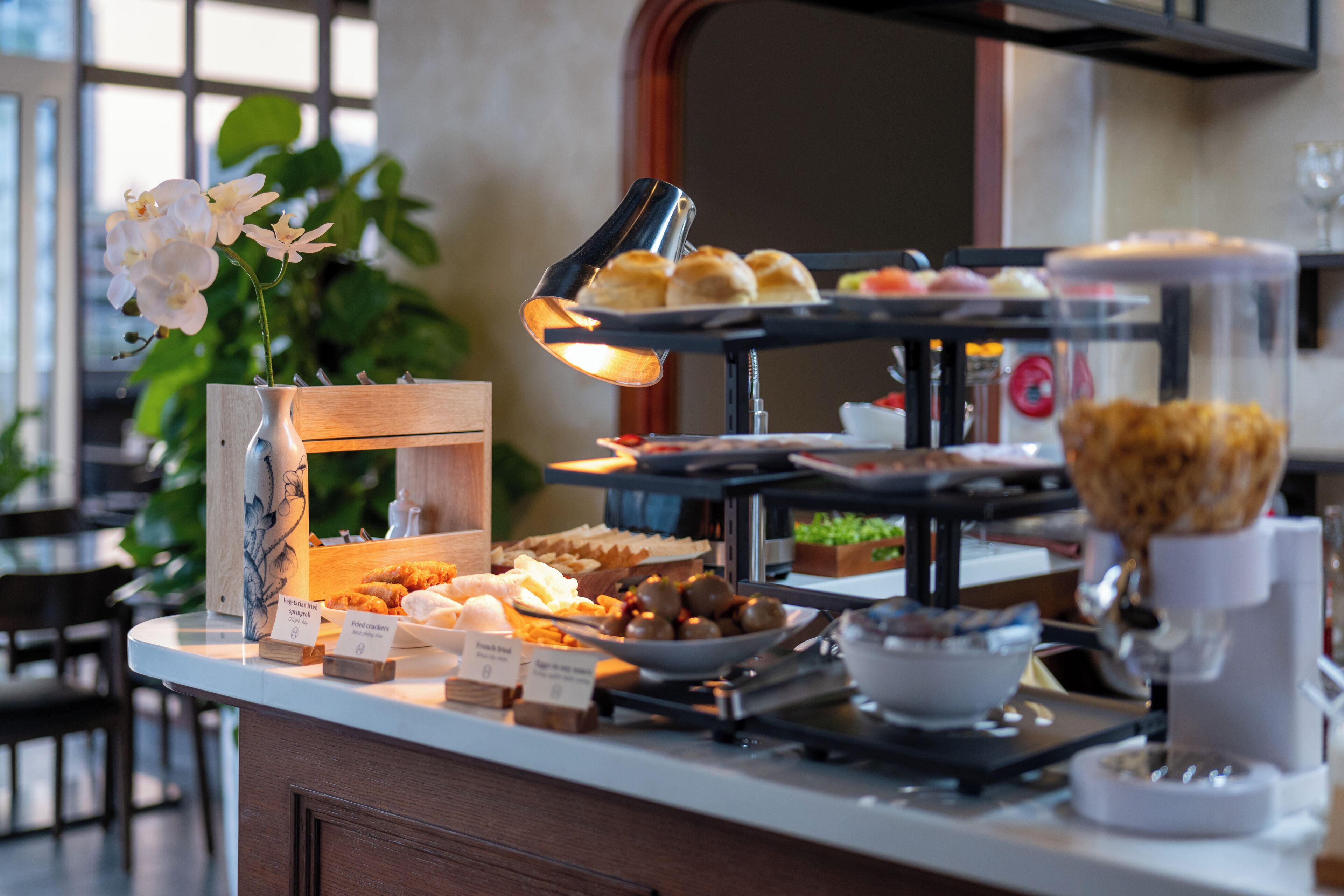 Un aparador de buffet amb diferents plats, una màquina de cafè i un ram de flors en un vas decoratiu.