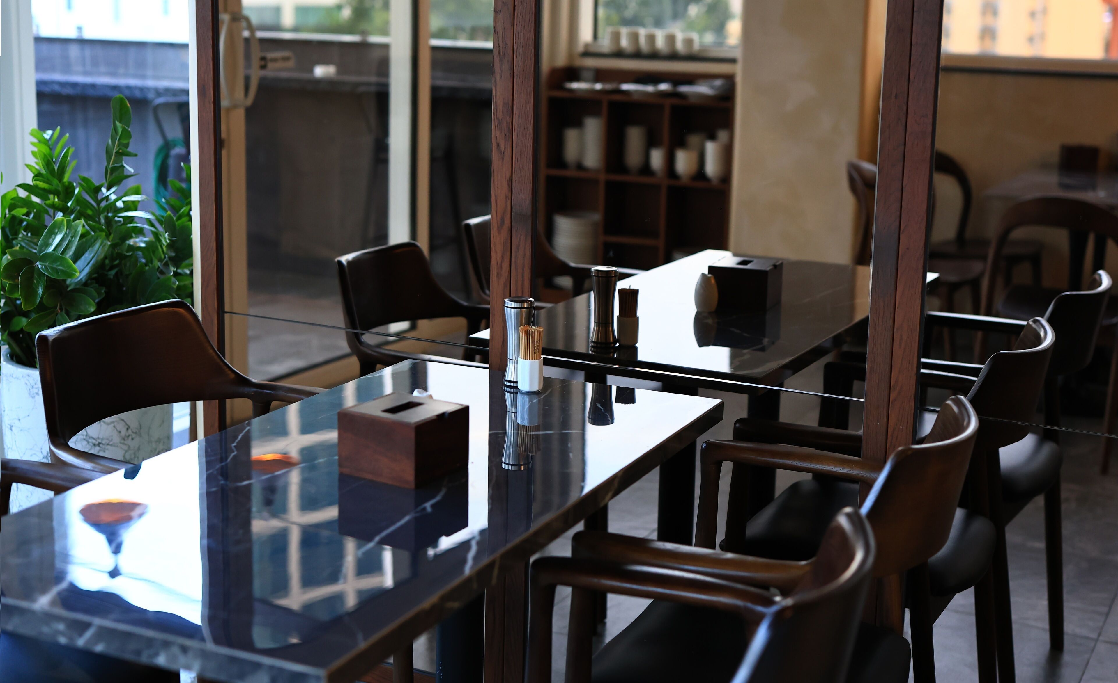 A modern restaurant interior with glass tables and wooden chairs.