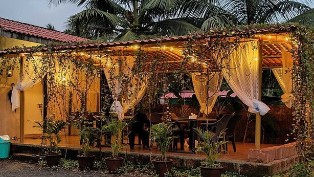 A cozy outdoor seating area with tables and chairs, surrounded by potted plants and draped with fabric. - O'NEST Countryside (Murud)